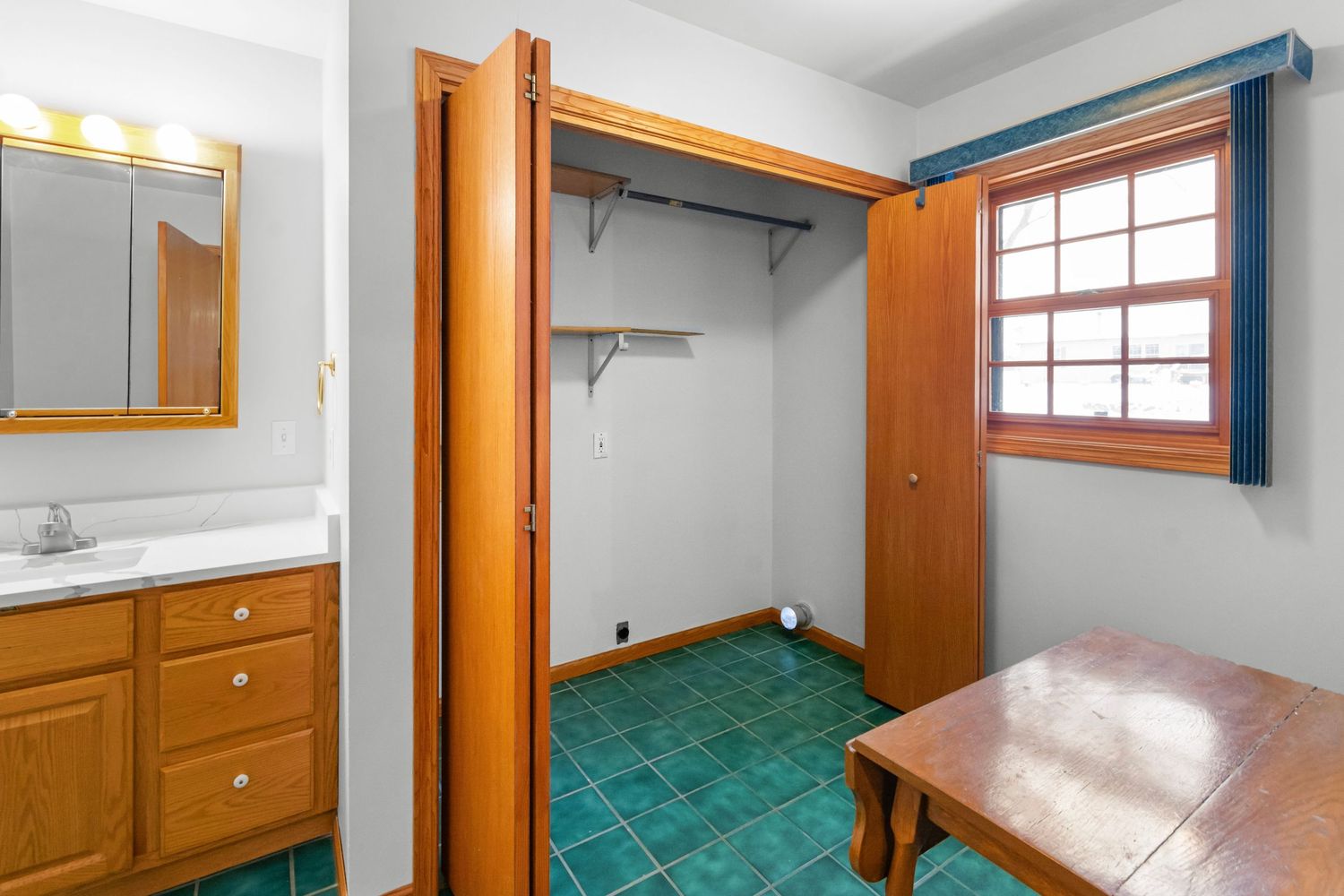 Small bathroom with turquoise tile floor, white walls, and wooden trim features a window and built-in storage cabinets.