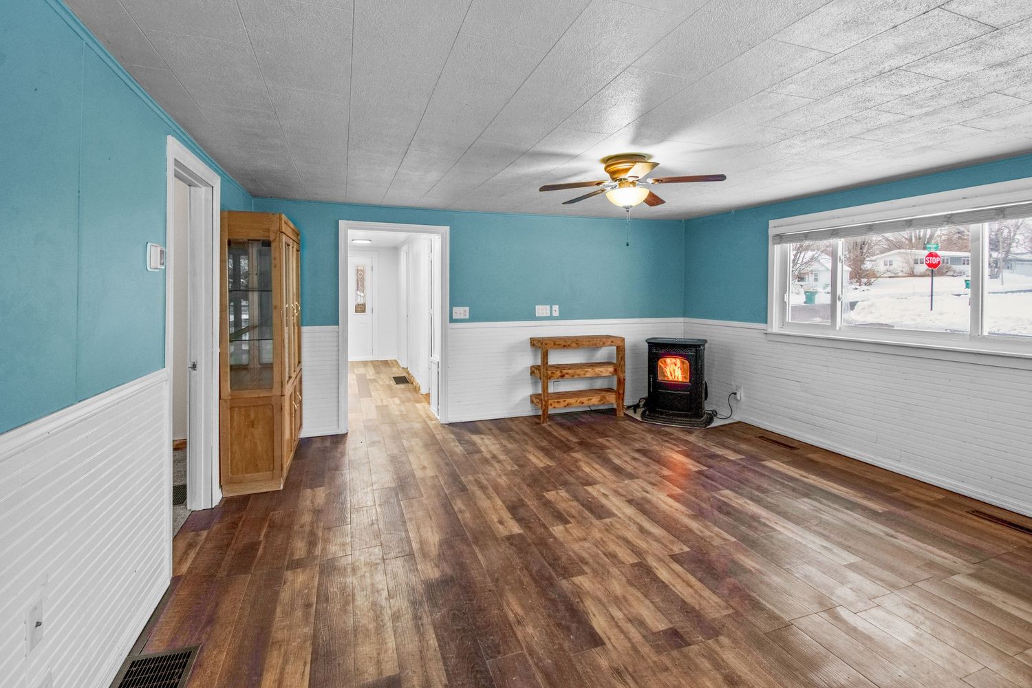 Large finished basement room with teal walls, hardwood flooring and ceiling fan.