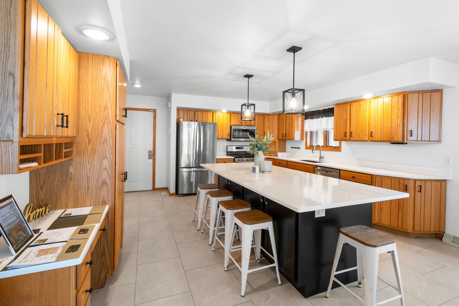 Modern kitchen with white countertops, wood cabinets, and pendant lighting shown in a panoramic view.