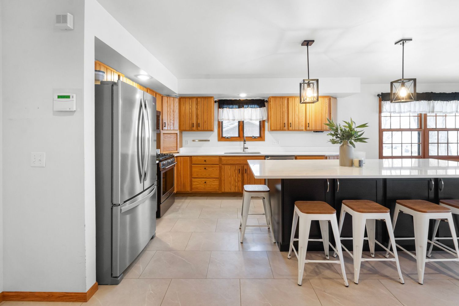 Modern white kitchen with stainless steel appliances, wood cabinets, and pendant lighting showcases an open concept design.