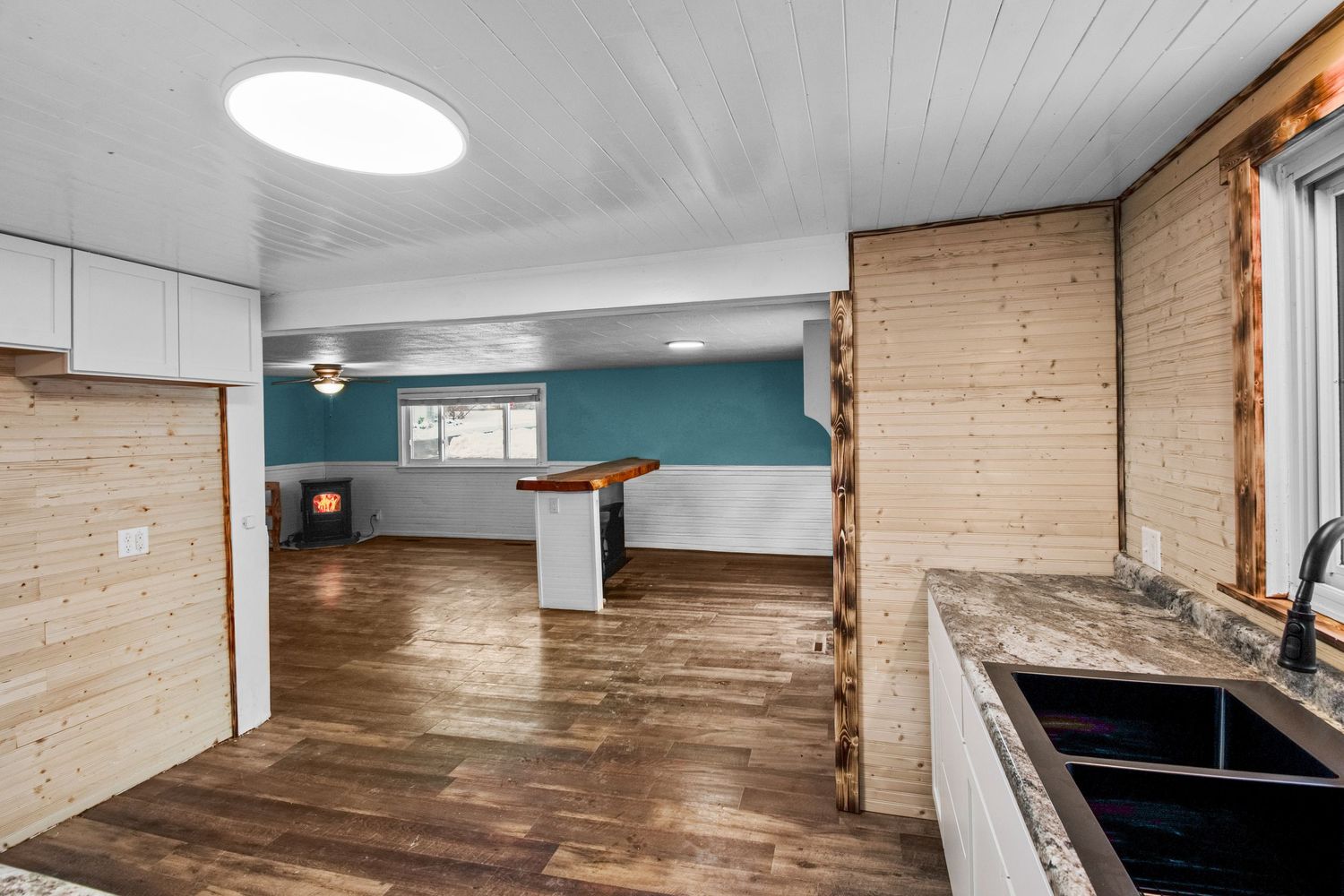 Open concept kitchen and living area with wood paneling and turquoise accent wall.