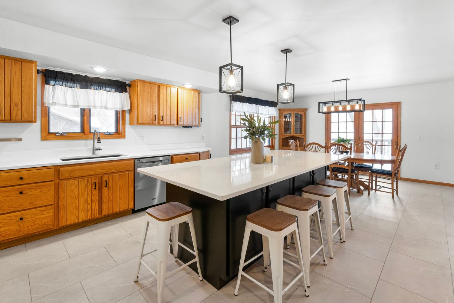 Modern open concept kitchen and dining area with wooden cabinets, white walls, and pendant lighting.