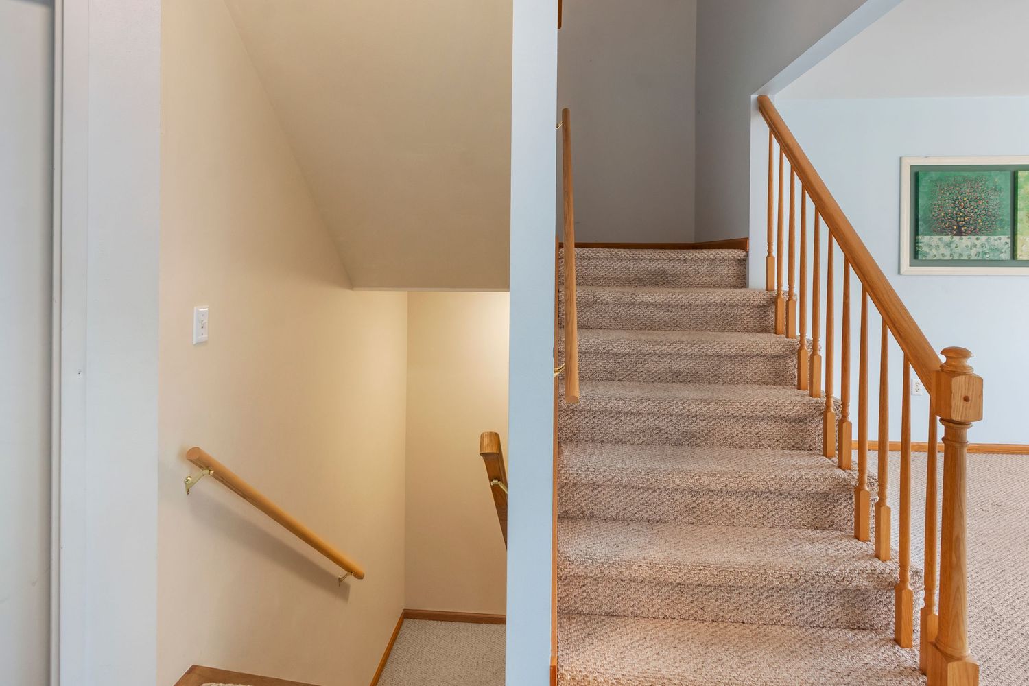 Carpeted staircase with wooden handrail and beige walls leading upstairs in modern home interior.