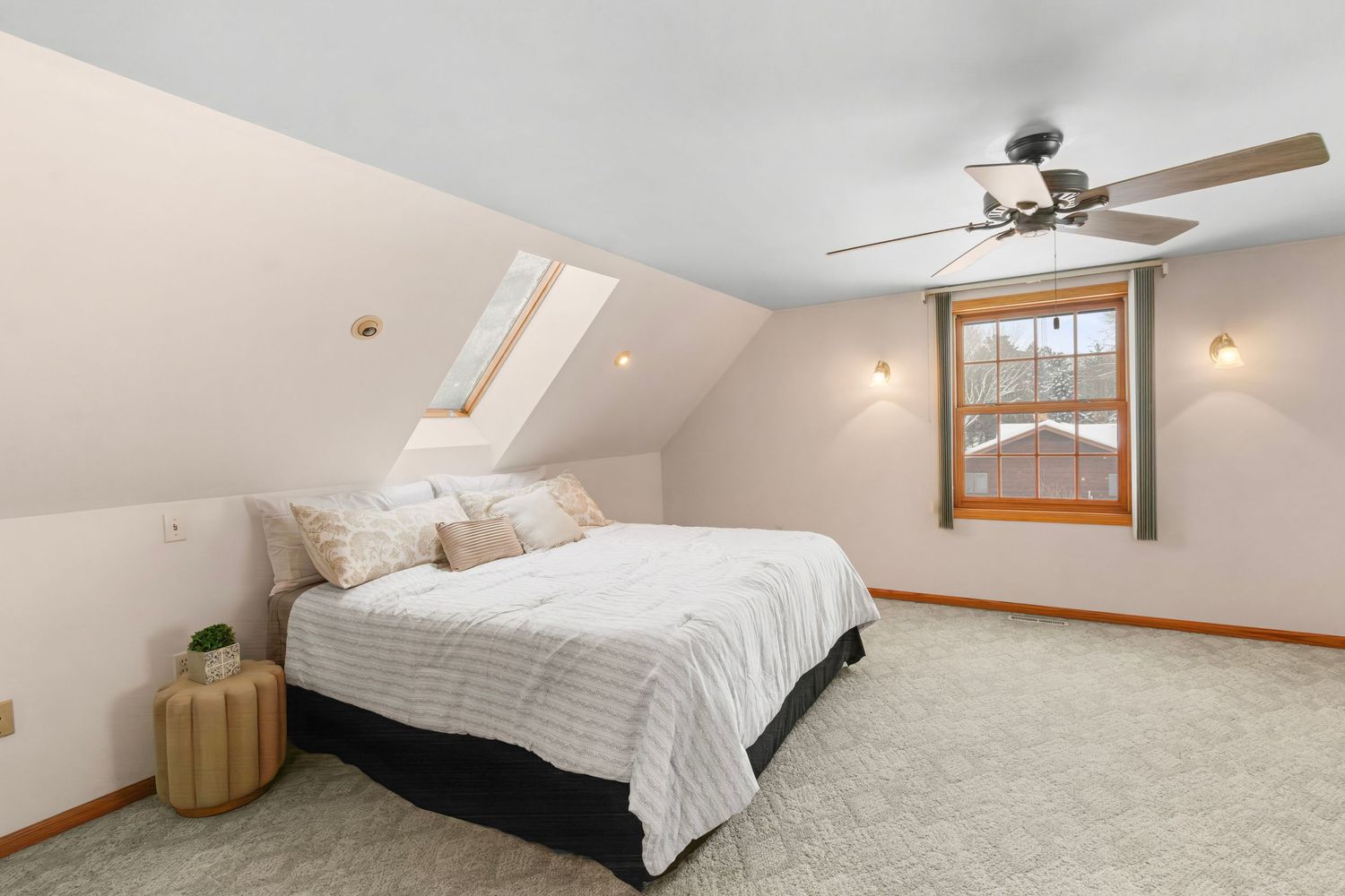 Cozy attic bedroom with sloped ceiling, carpeted floor, and natural light streaming through wood-framed windows.
