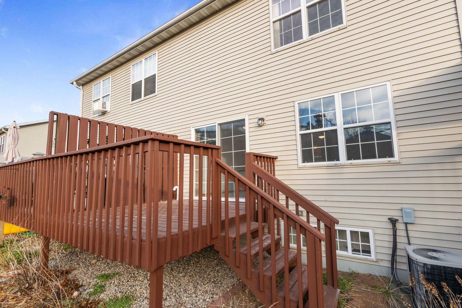 Side view of beige house with elevated wooden deck and multiple windows.