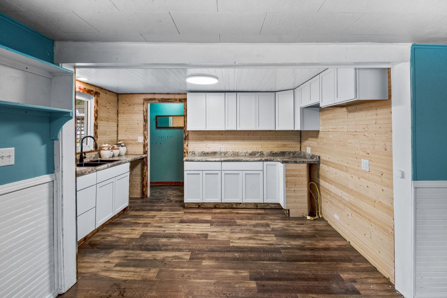 L-shaped kitchen with white cabinets, wood walls, and turquoise accent color.