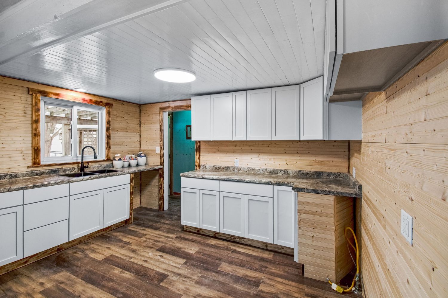 Modern kitchen with white cabinets, wood paneled walls and hardwood flooring in rustic style.