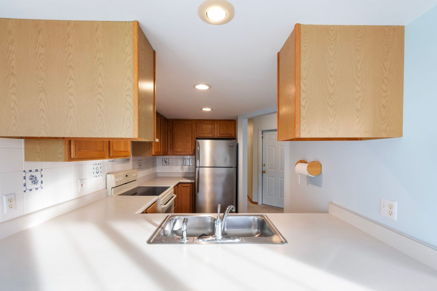 Modern kitchen interior with light wood cabinets, stainless steel appliances, and recessed lighting.