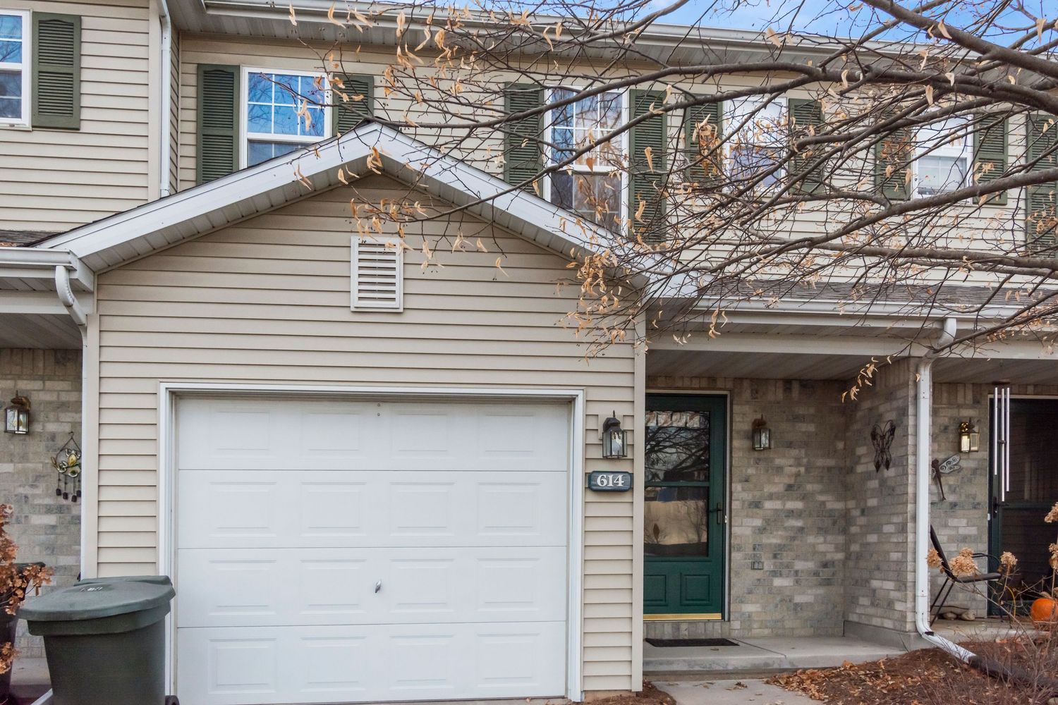 Exterior view of a beige suburban house with white garage door and black shutters in winter.