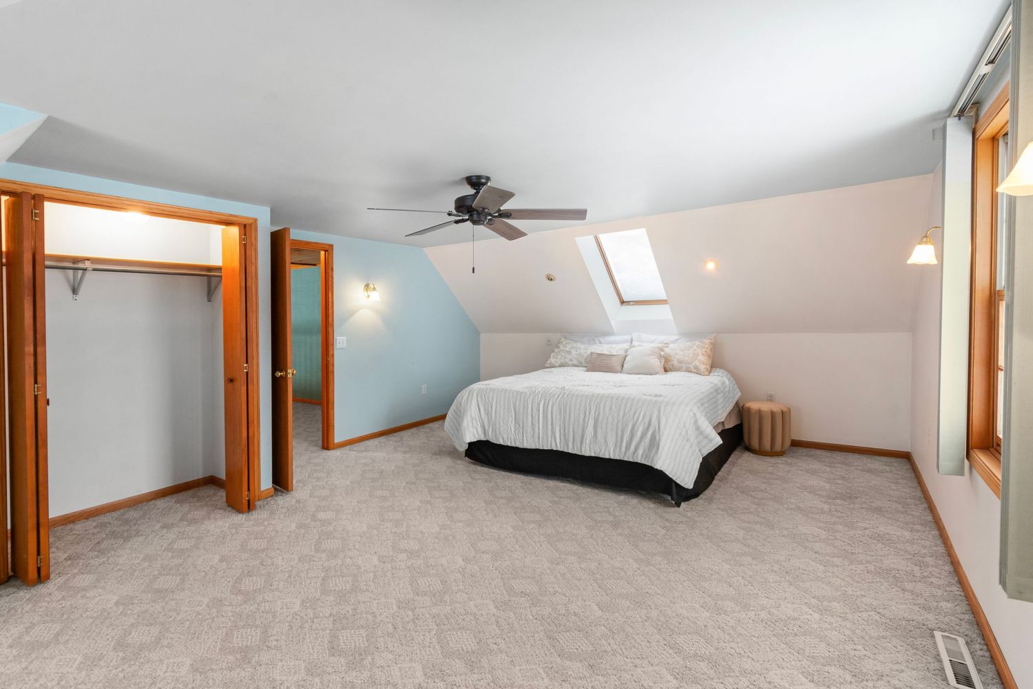 Spacious carpeted bedroom with sloped ceiling, skylights and large windows.