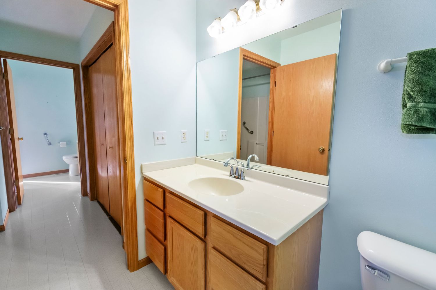 Bathroom vanity with large mirror, wooden cabinets, and light blue walls.