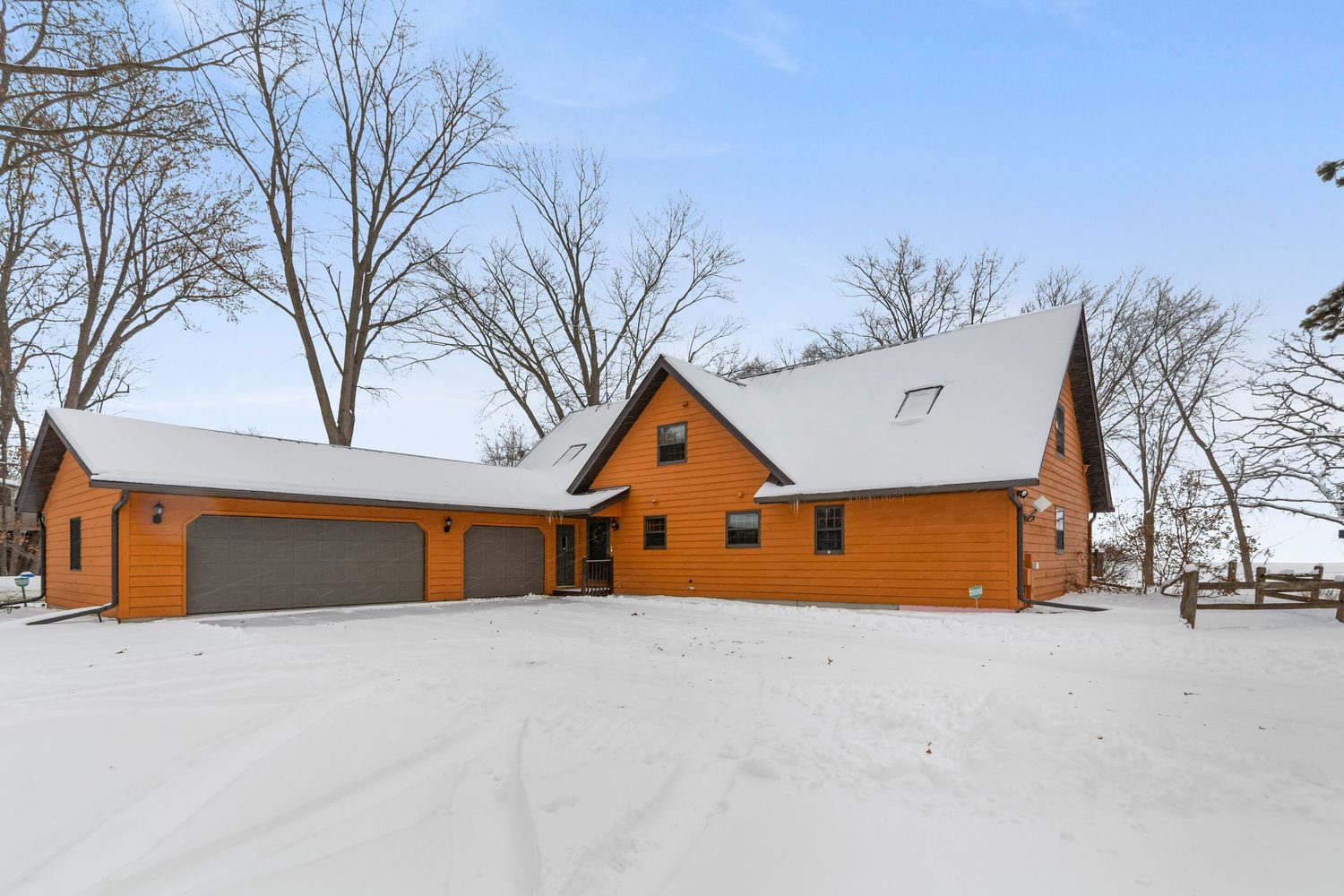 Snow-covered landscape with orange log cabin style house and detached garage visible among bare winter trees.
