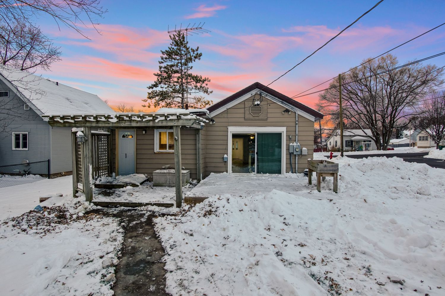 Snow-covered property with ranch-style houses and utility poles against a pink and purple sunset sky.