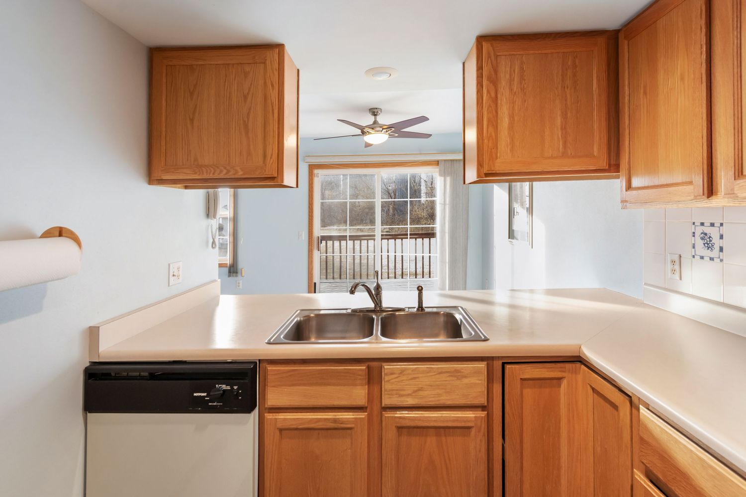 Modern kitchen interior with honey oak cabinets, white countertops, and ceiling fan in natural lighting.