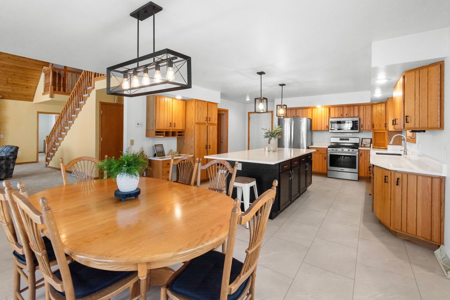 Spacious dining room connected to kitchen featuring wooden table and modern lighting fixtures.
