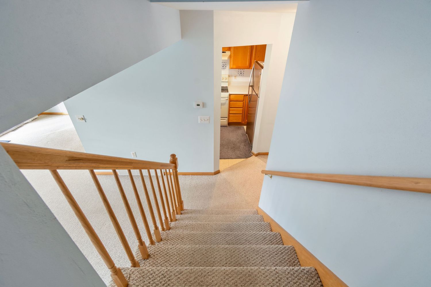 Carpeted staircase with wooden handrail and white walls leading upstairs in residential home.