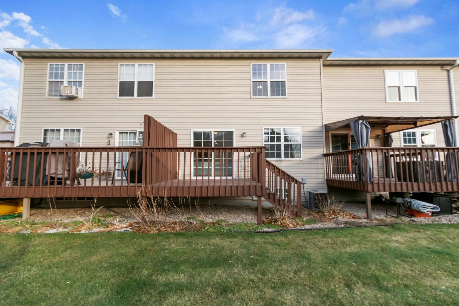 Rear exterior view of tan vinyl sided house with wooden deck and landscaped yard.