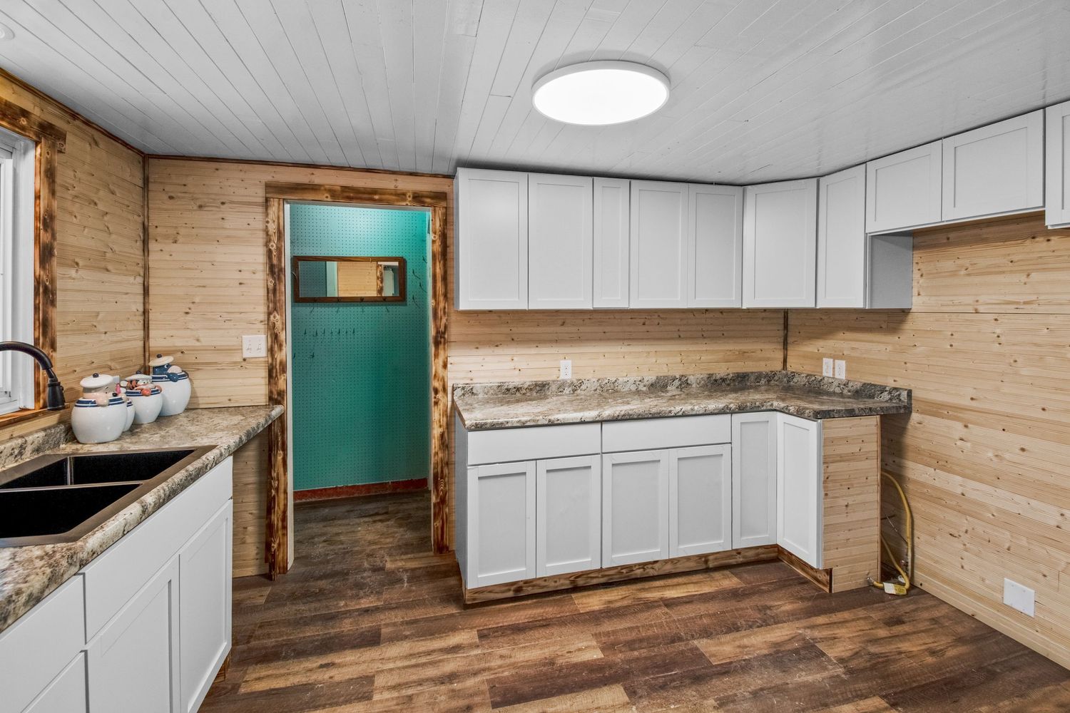 Kitchen interior with white cabinets, retro turquoise refrigerator, and wood-paneled walls.