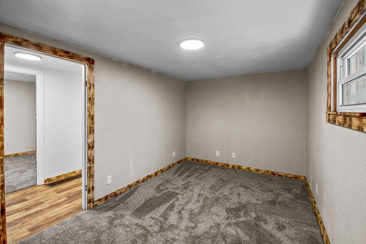 Newly renovated room with gray carpet flooring and recessed lighting in ceiling.