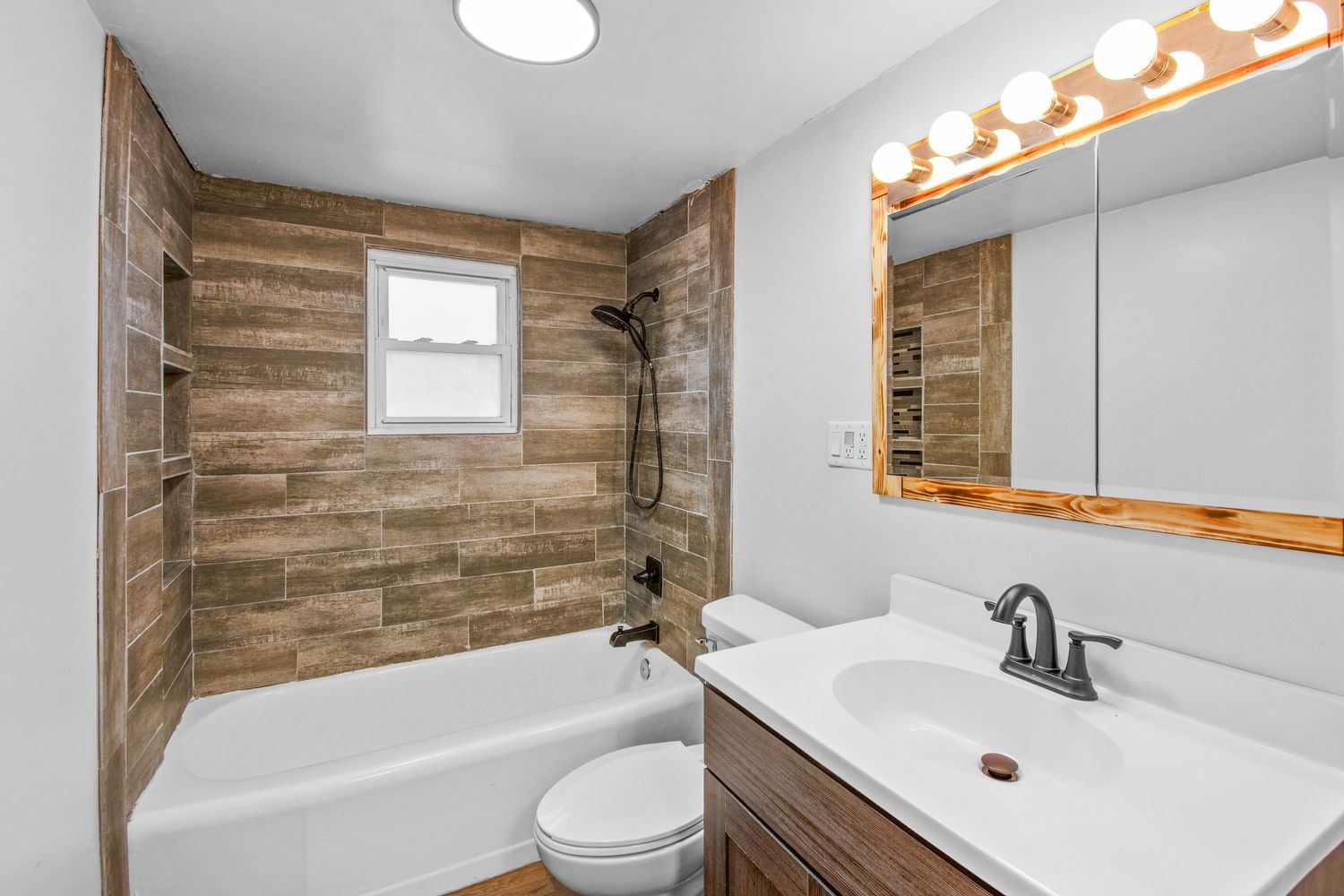 Modern bathroom with wood accent wall, white vanity, and bright vanity lights above a large mirror.