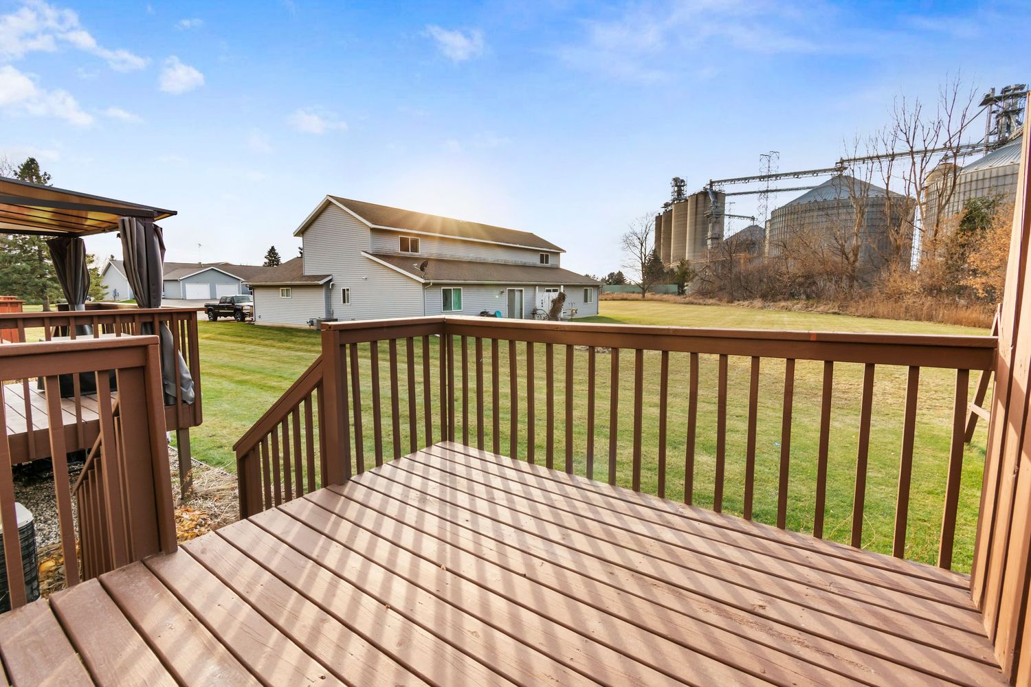 Panoramic view of a wooden deck with railing overlooking a grassy backyard on a sunny day.