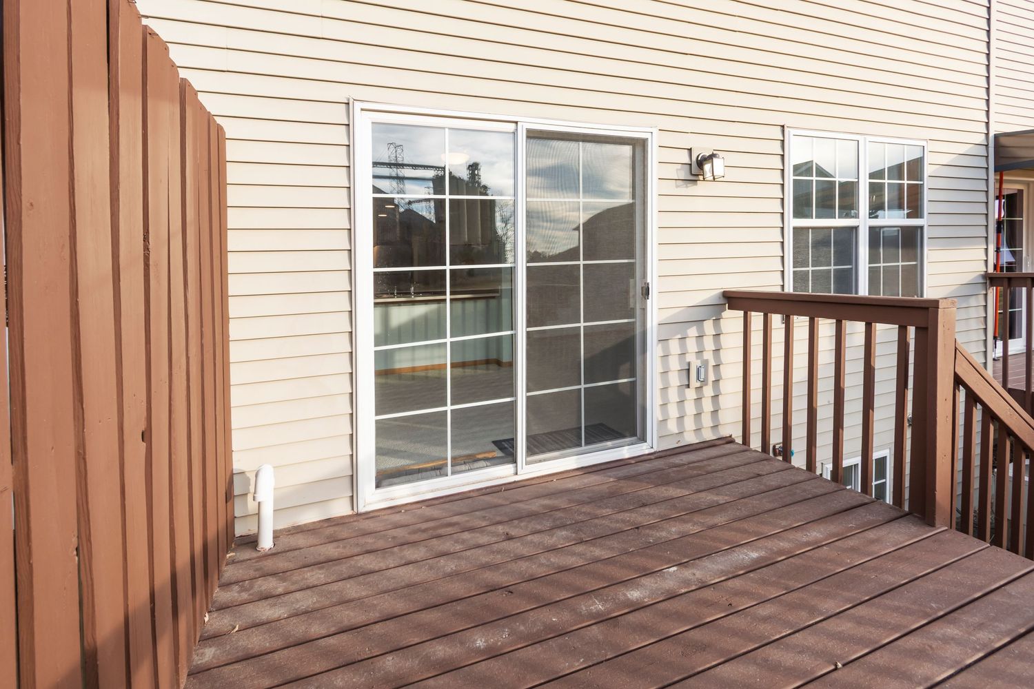 Close-up view of wooden deck with railing attached to beige sided house.
