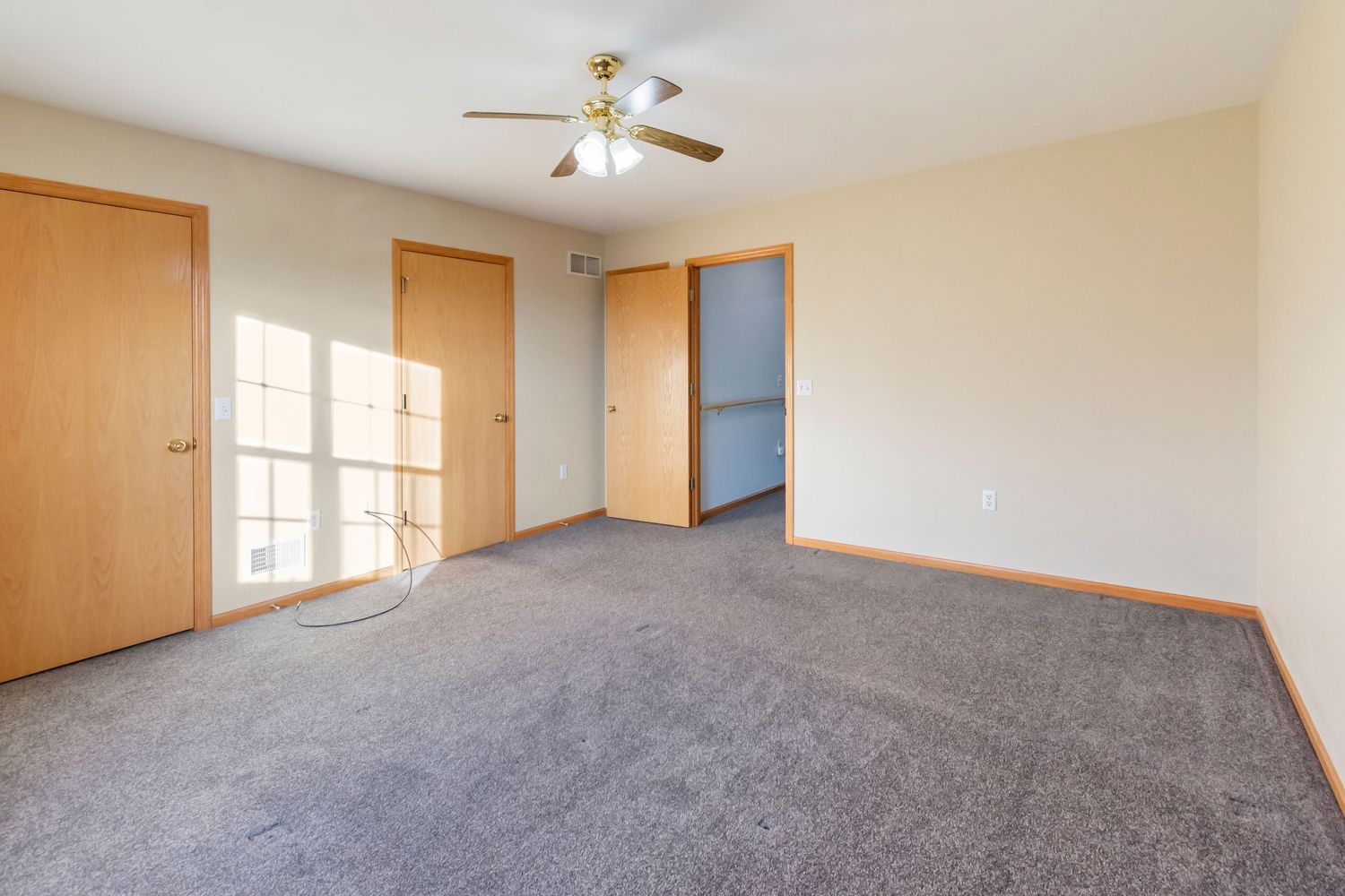 Spacious empty room with grey carpeting, wooden doors, and ceiling fan.