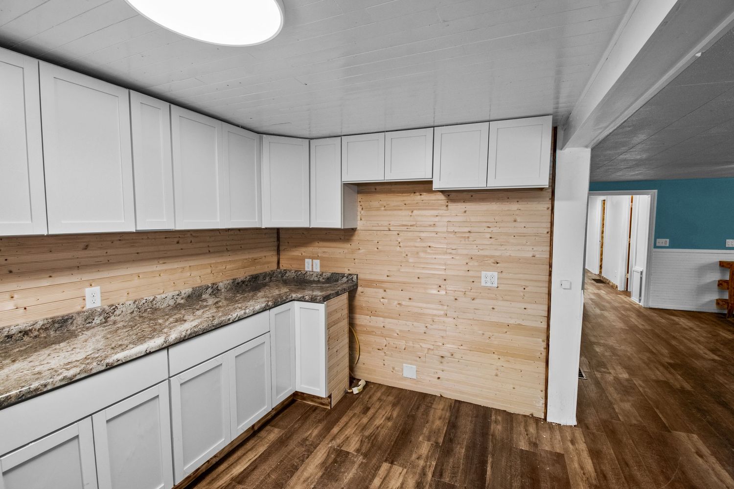 Long hallway with white walls, ceiling lights, and hardwood flooring extending to living space.