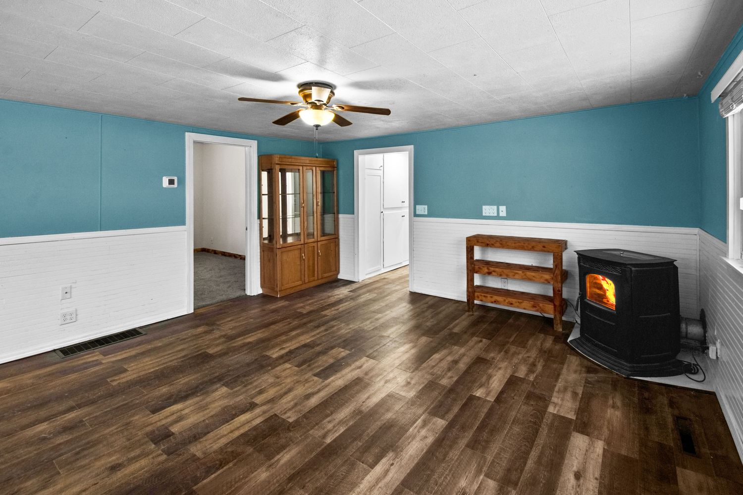 Spacious room with teal walls, white wainscoting, wood floors and a freestanding stove.