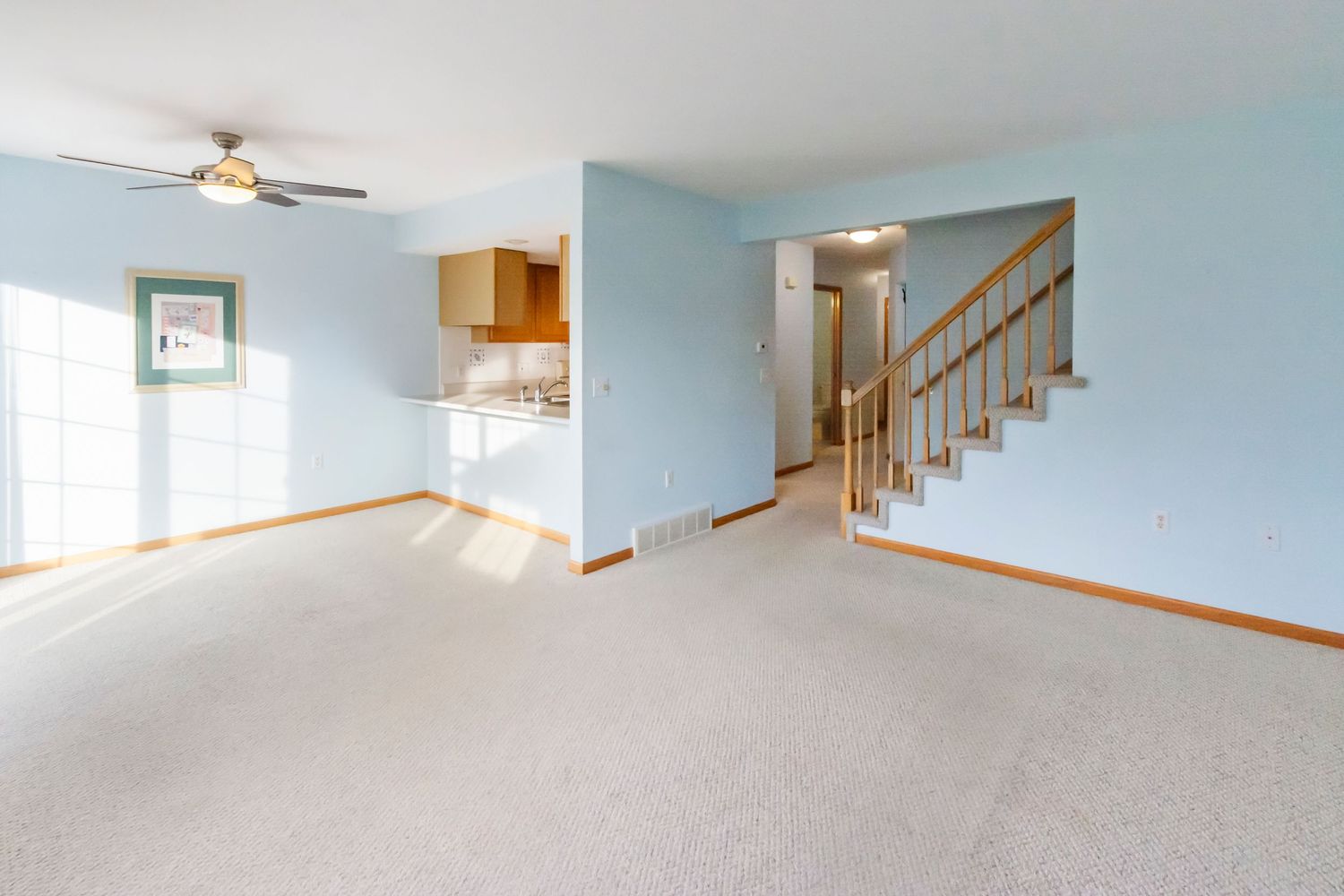 Large open living space with light blue walls, ceiling fan, and natural lighting.