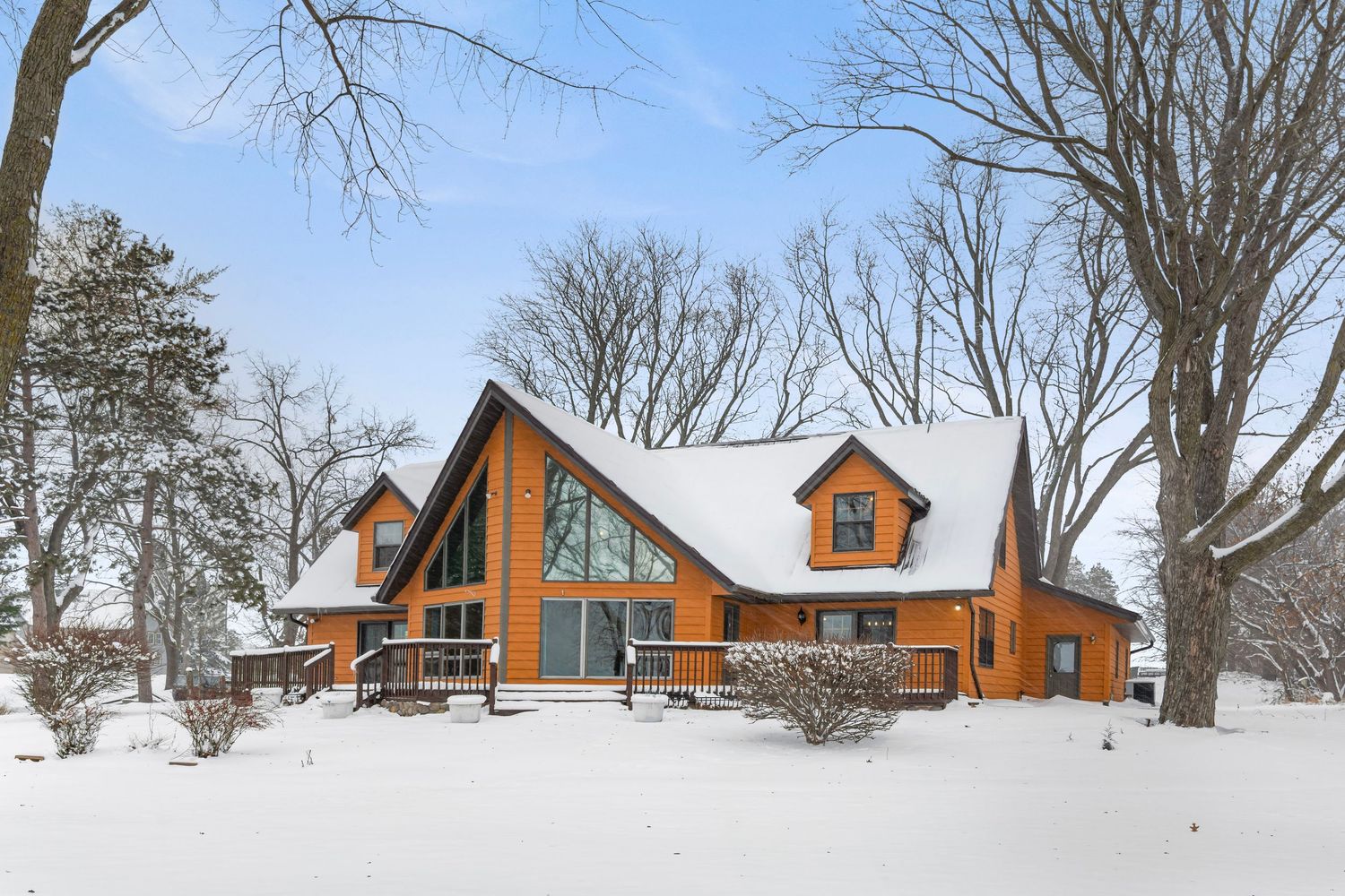 Snow covered rustic cabin homes with orange wood siding nestled among bare winter trees.