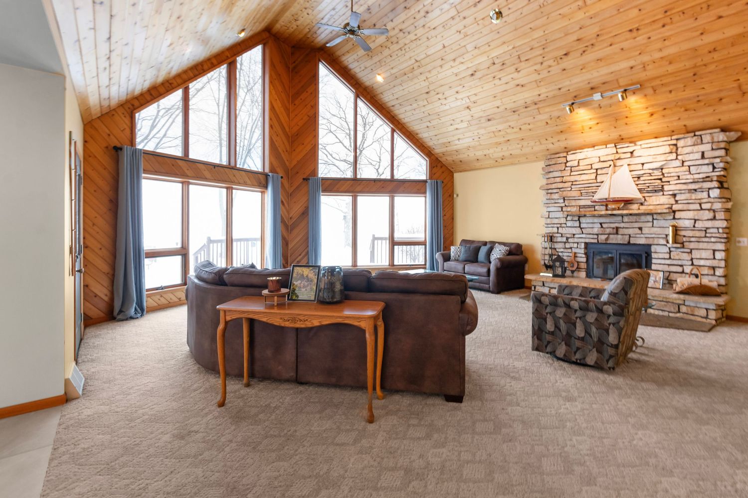 Large rustic living room with vaulted wood ceiling, stone fireplace, and panoramic windows offering natural light.