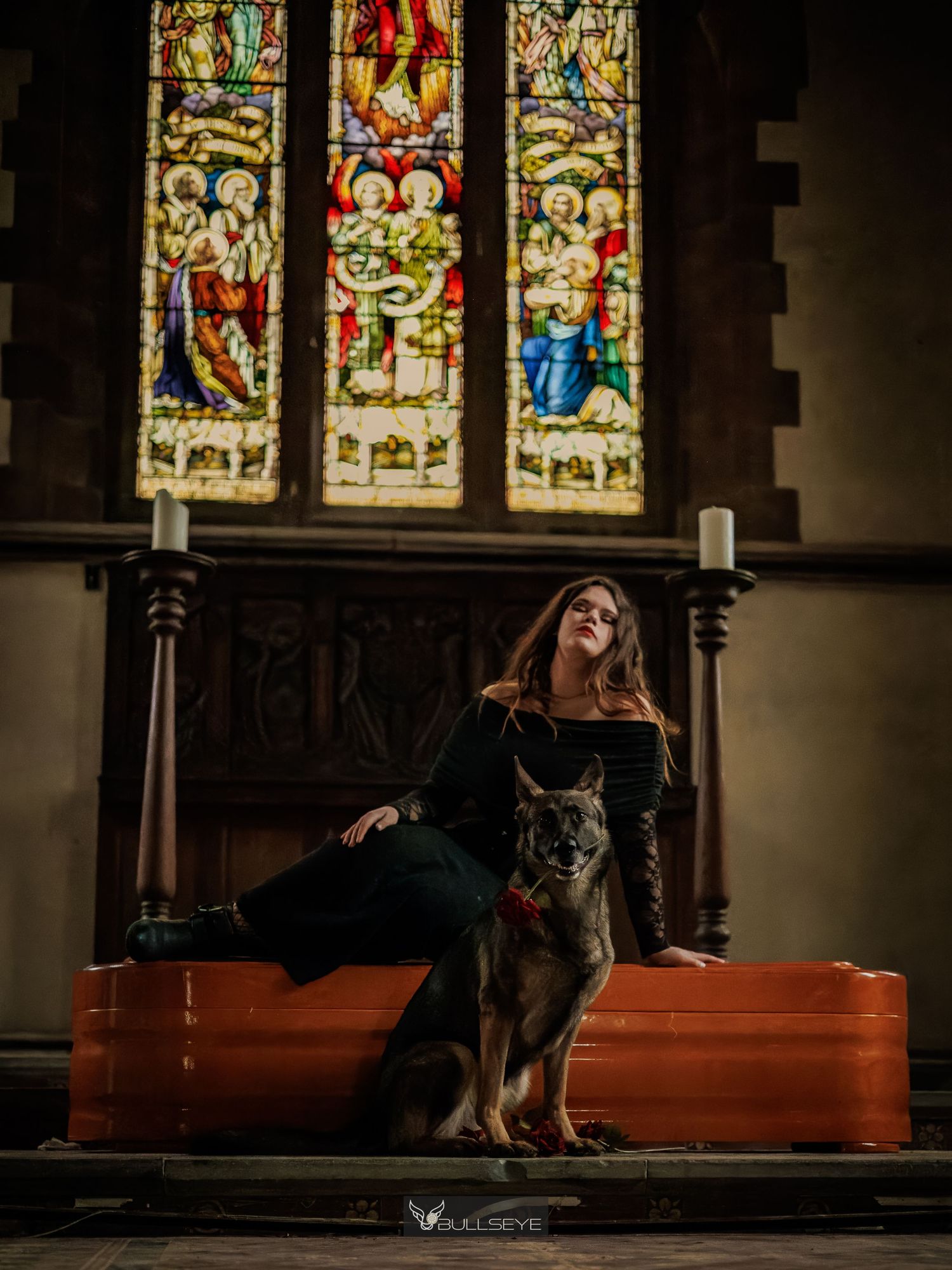 Woman in black outfit poses with German Shepherd dog inside historic church with ornate stained glass windows.