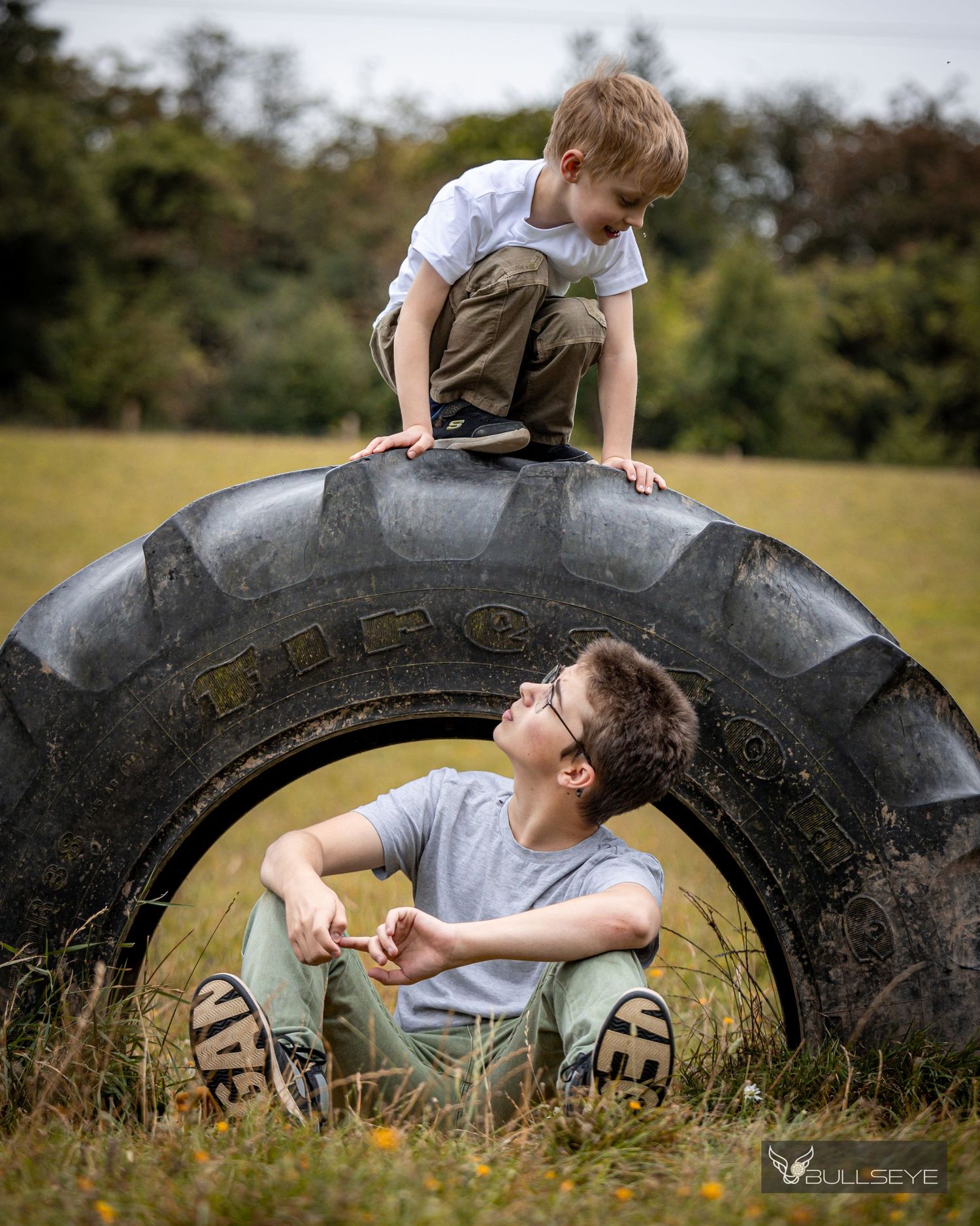 Children playing and climbing on large tractor tire in rural field setting.