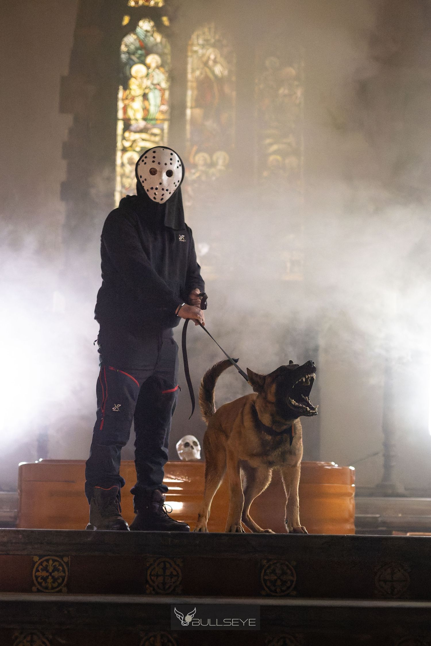 A Belgian Malinois dog on a leash in a misty church with stained glass windows.
