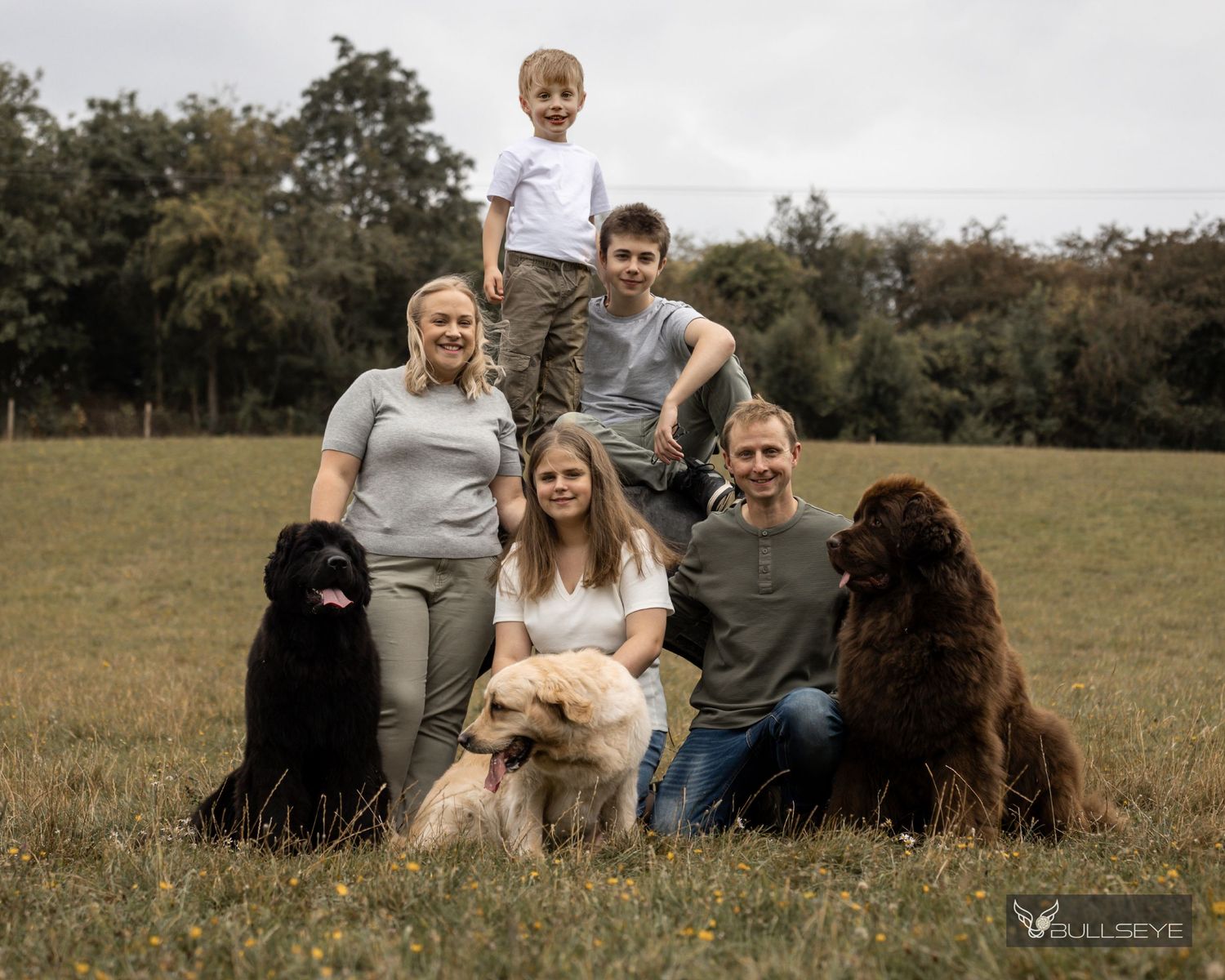 Group relaxing outdoors with pets in grassy field on autumn day.