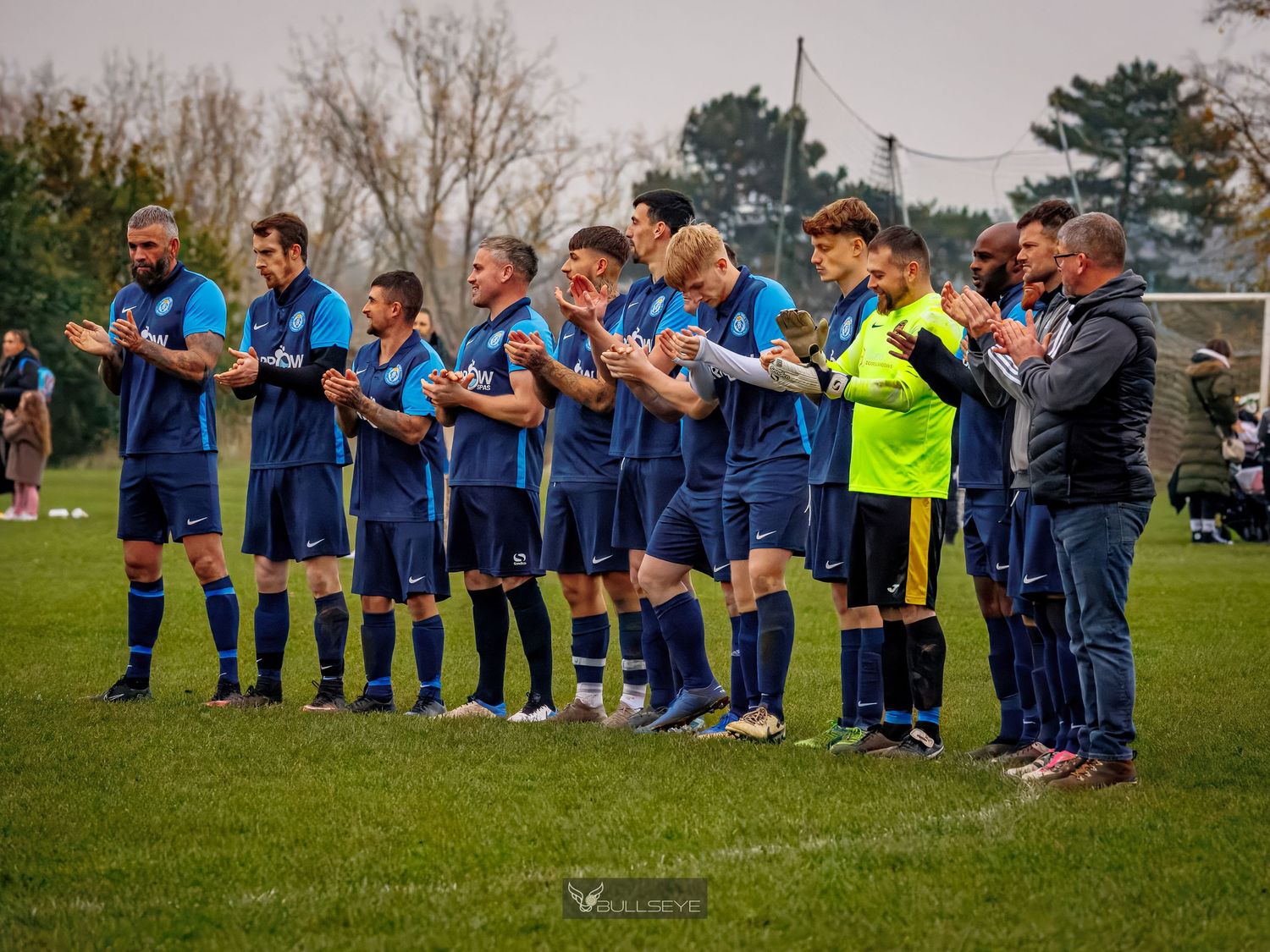 Soccer team in blue uniforms stands in line on grass field during pre-game ceremony.