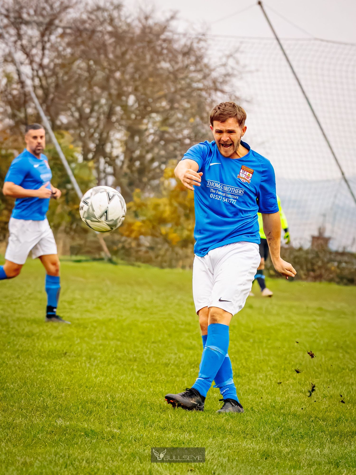 Soccer player in blue jersey kicks the ball on a grassy field during an amateur match.