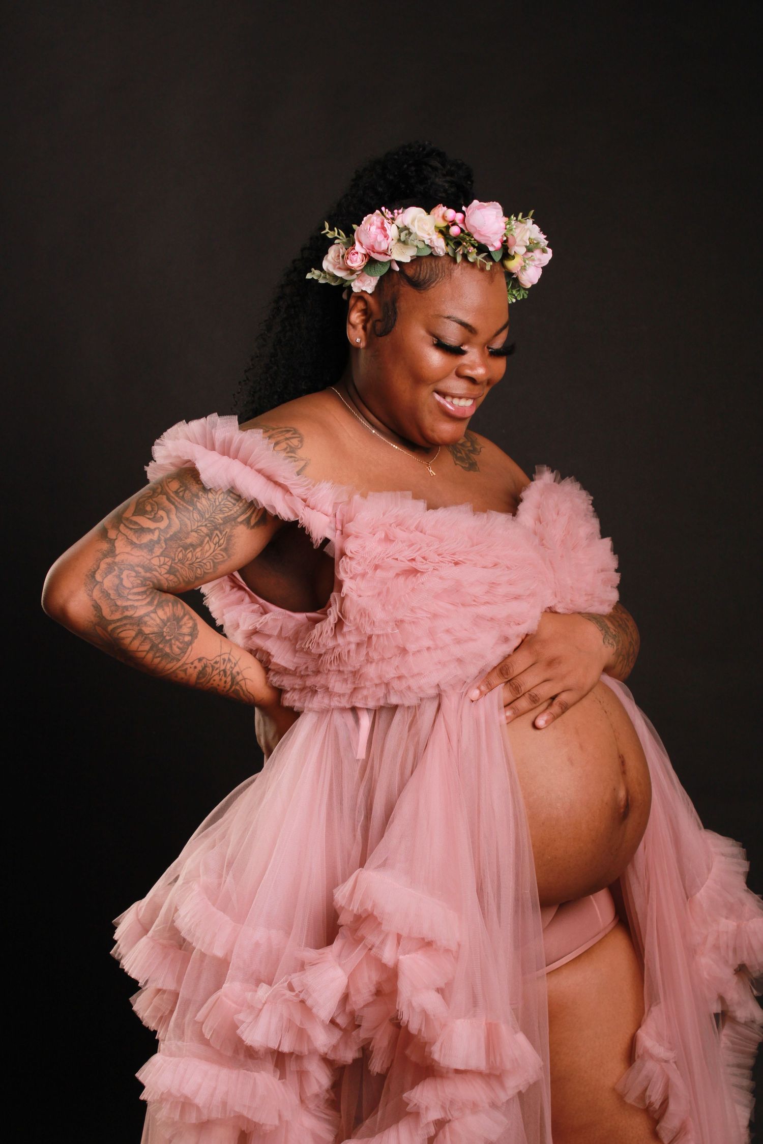 Dramatic maternity portrait featuring flowing pink dress and floral headpiece.