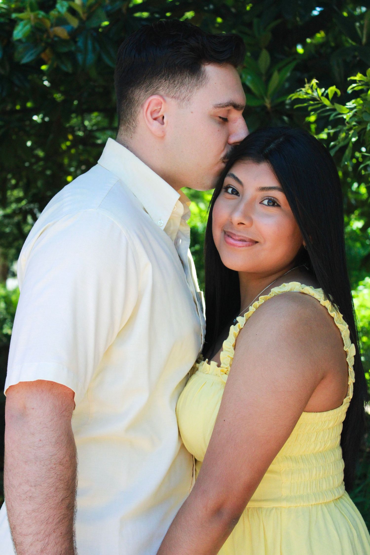 Couple in yellow dress and white shirt sharing tender moments outdoors.