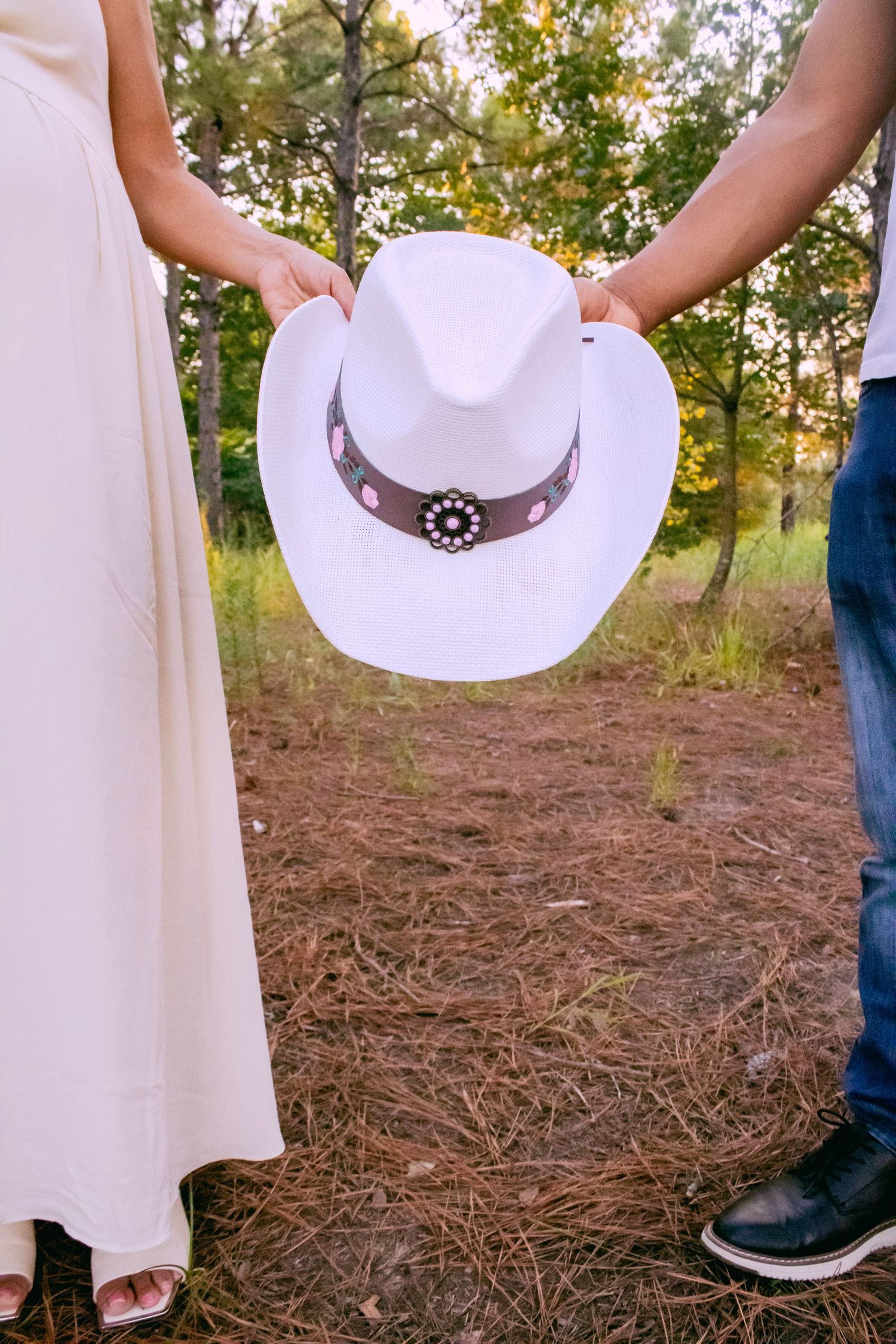 White cowboy hat held between two people in outdoor setting.