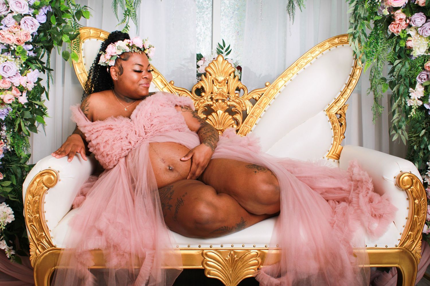 Maternity photoshoot featuring a pink tulle robe and floral crown against a light background.