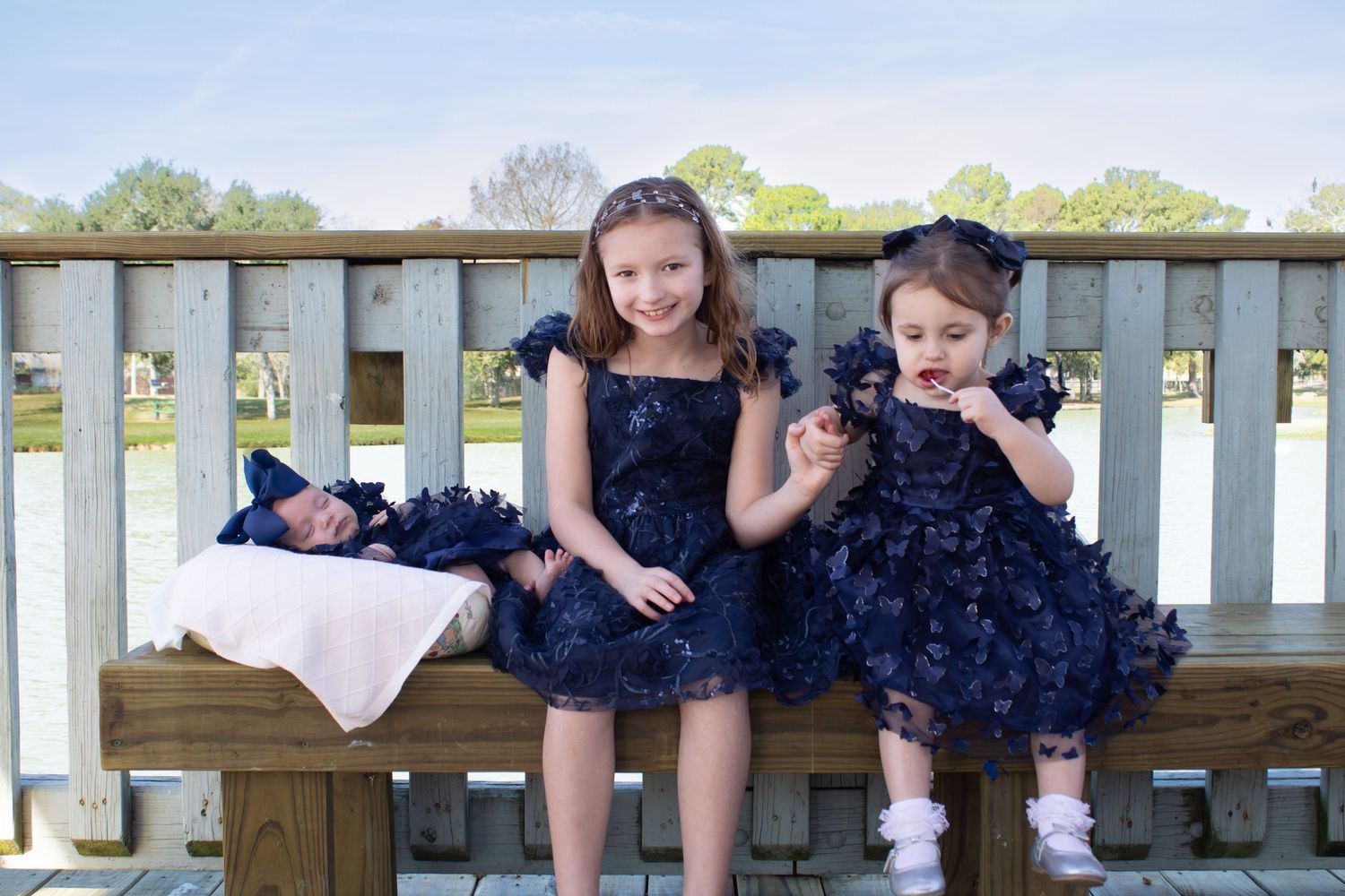 Two children in navy lace dresses sitting on wooden deck railing.