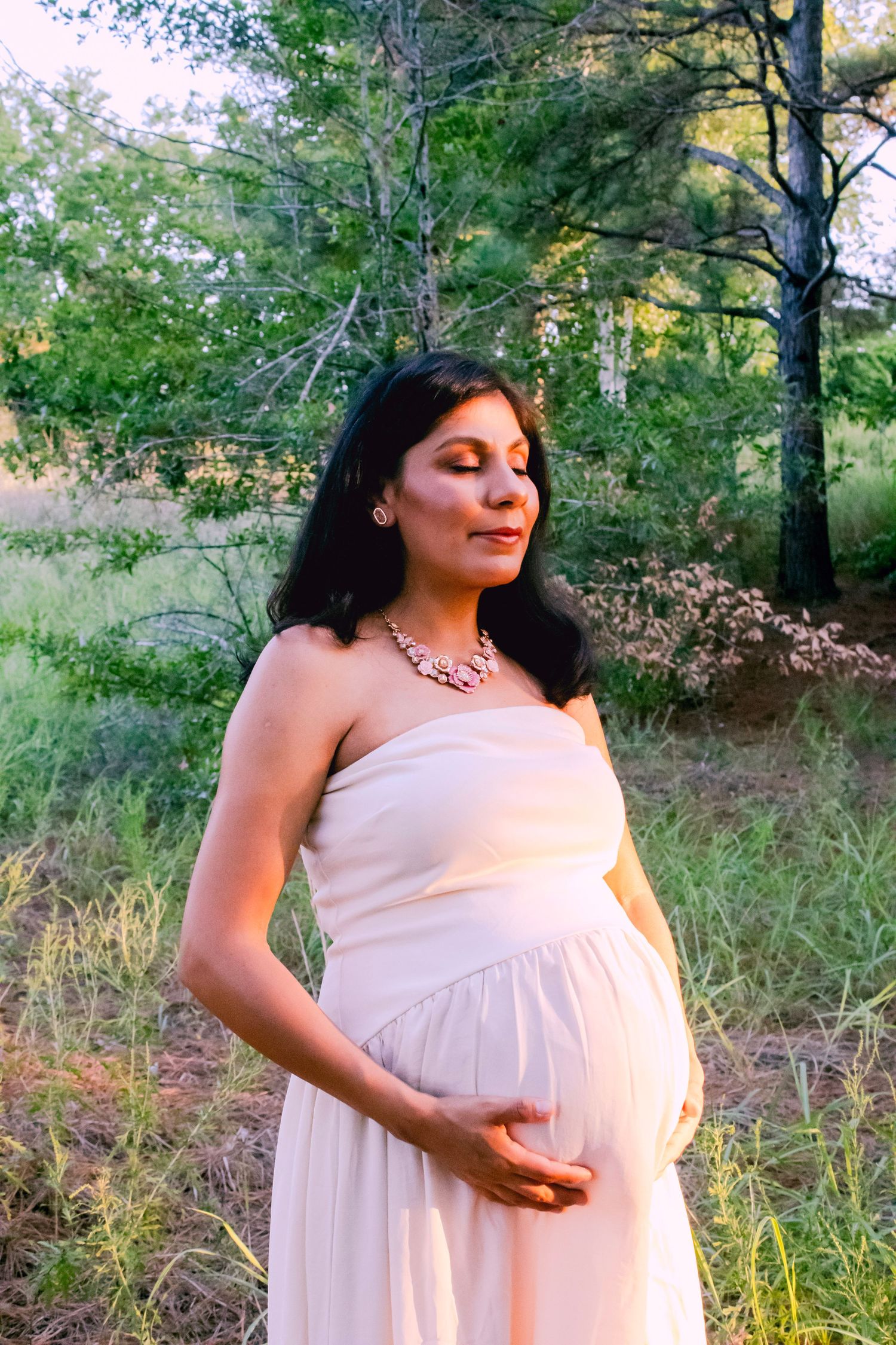A peaceful maternity portrait taken in a natural outdoor setting with pine trees.