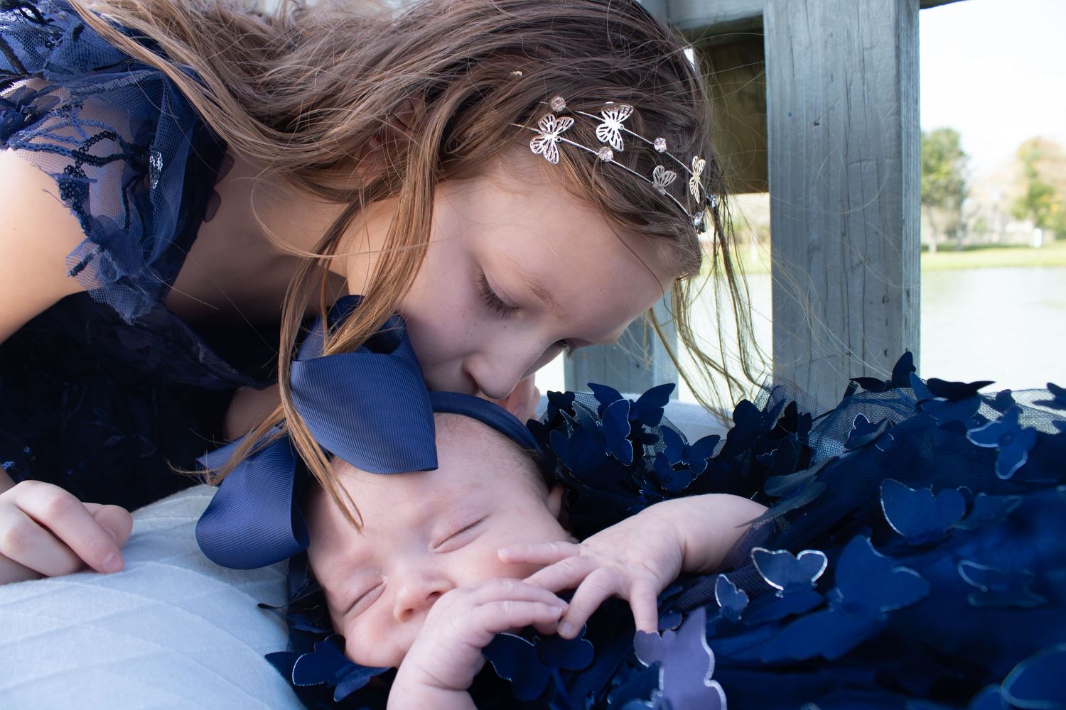 Sweet moment between siblings in navy dresses on outdoor deck.