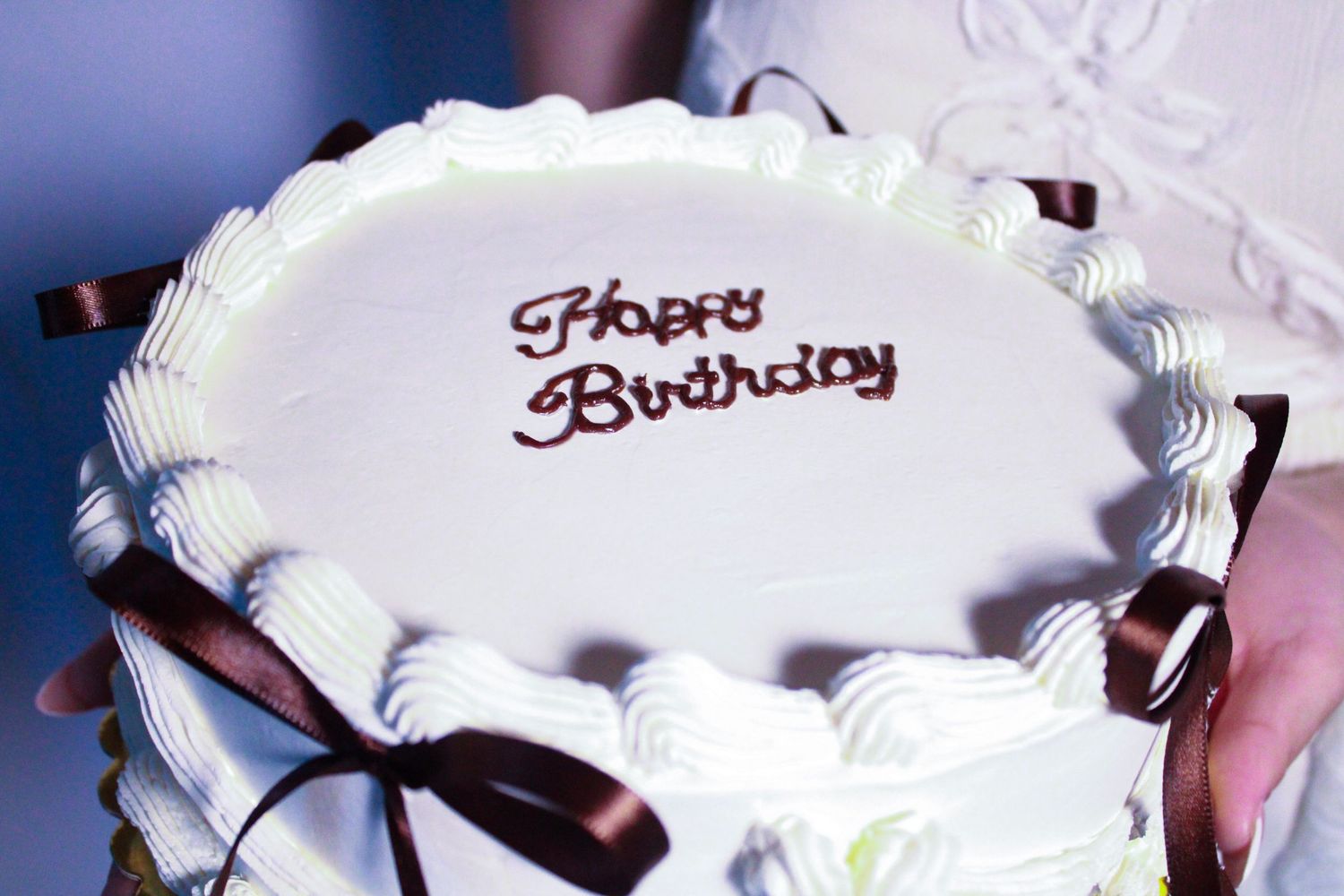 Close-up shots of a white birthday cake with brown ribbon decorations.