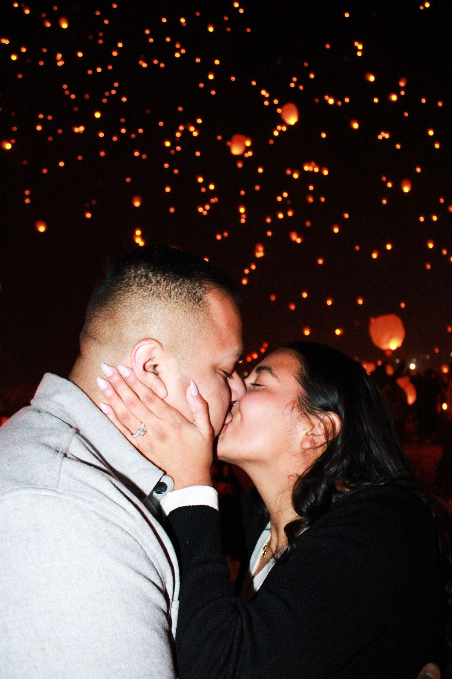 Romantic kiss under glowing orange lanterns floating in night sky.