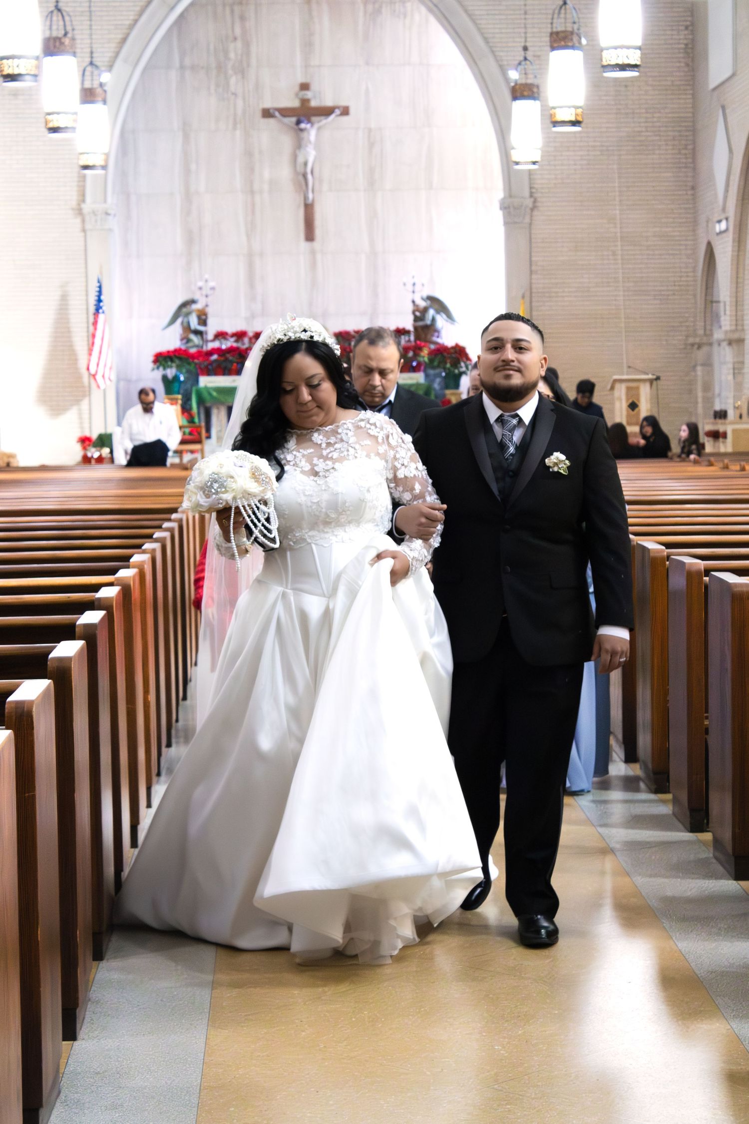 A wedding couple walking down the church aisle with wooden pews and hanging lights.