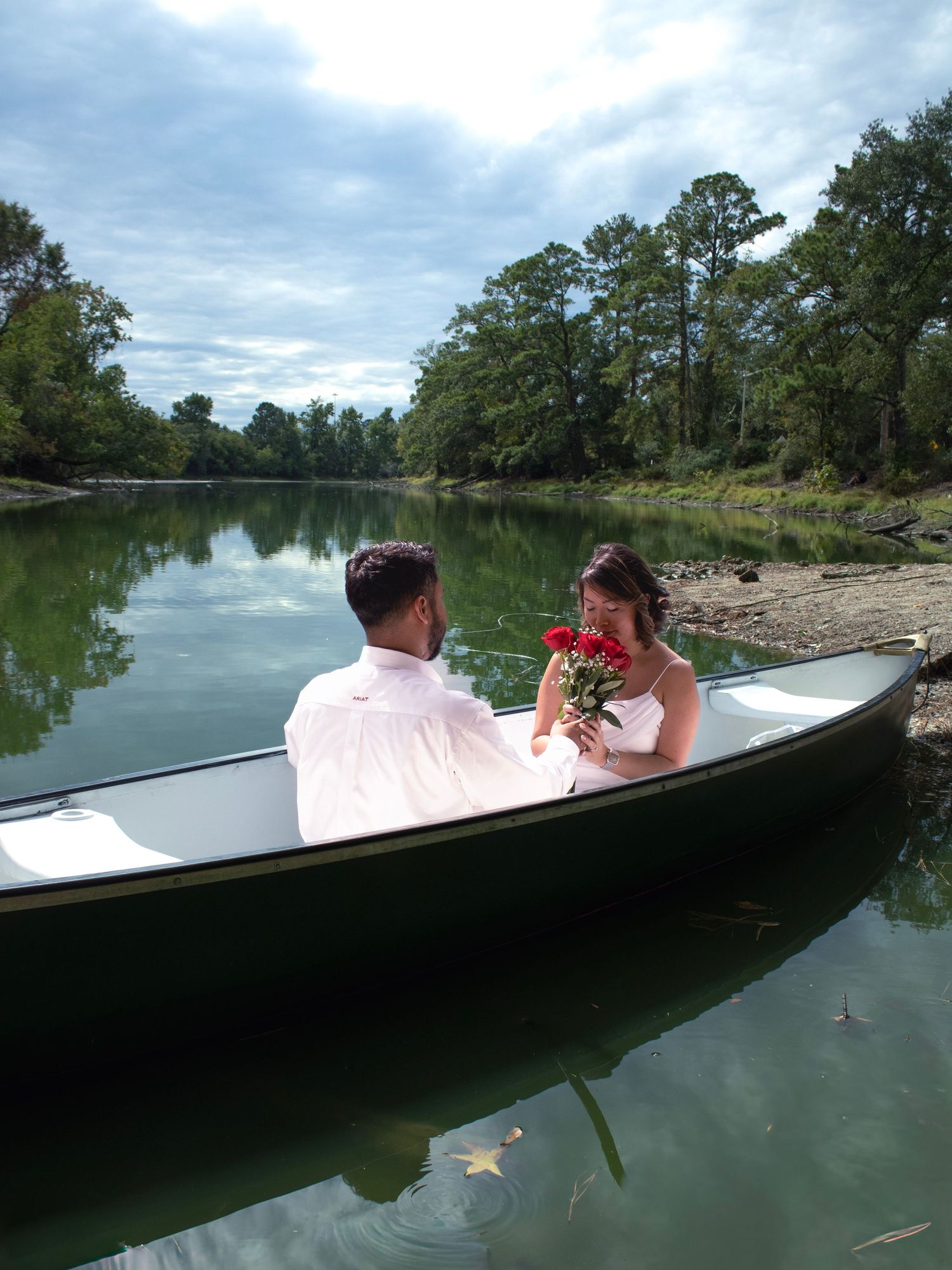 A couple sharing romantic moments in a boat on a serene lake surrounded by trees.