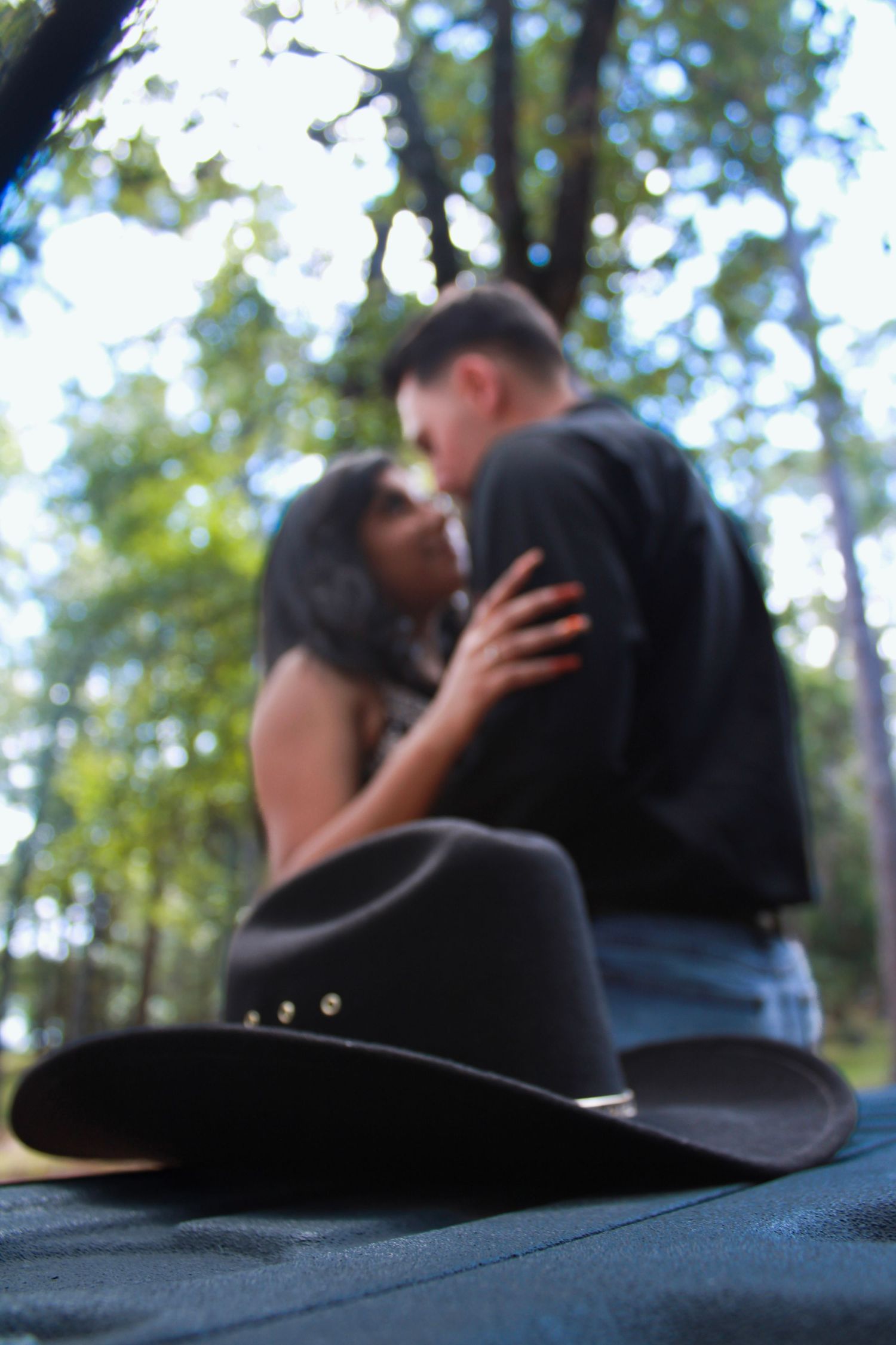 A black cowboy hat sits in focus while a couple embraces in the blurred background.